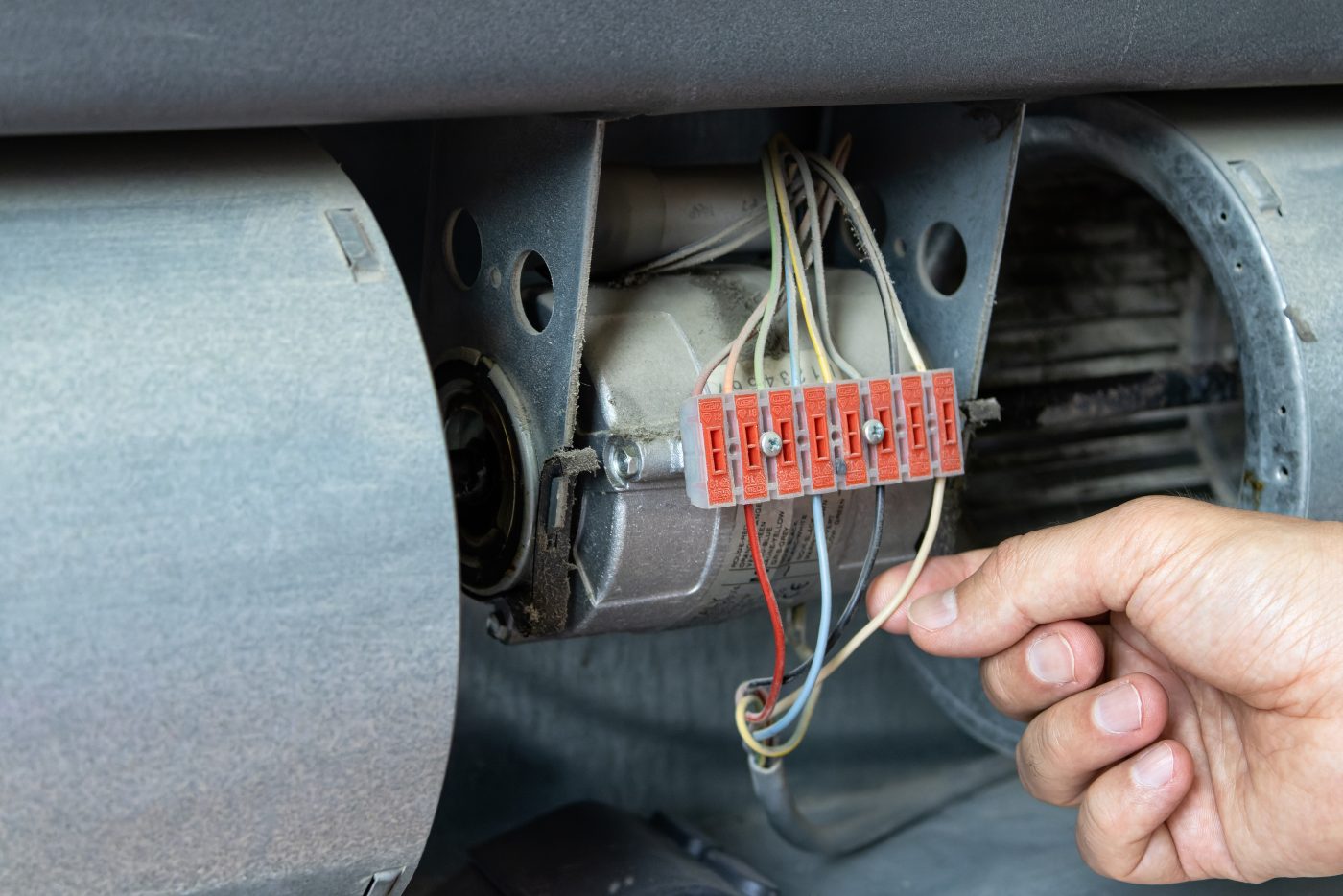 NCIS technician reconnecting the wiring on a furnace blower motor during a heating repair.