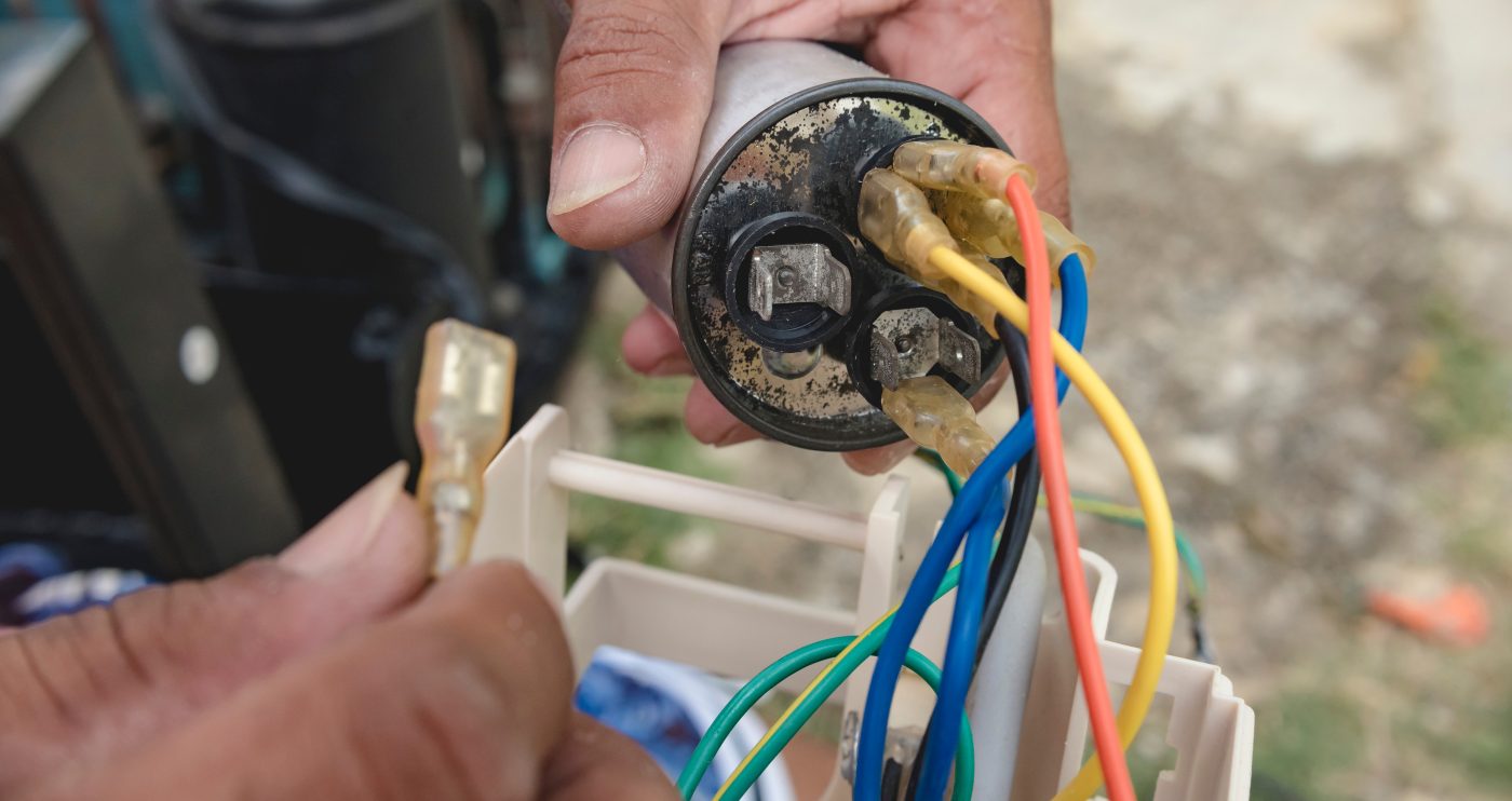 Technician holding a generator run capacitor during a repair, representative of generator troubleshooting.