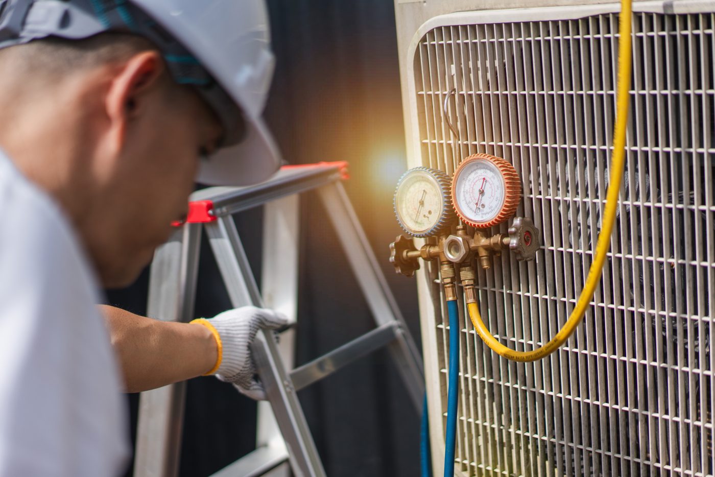 NCIS technician checking an air conditioner from a ladder, representative of NCIS heating and cooling services.