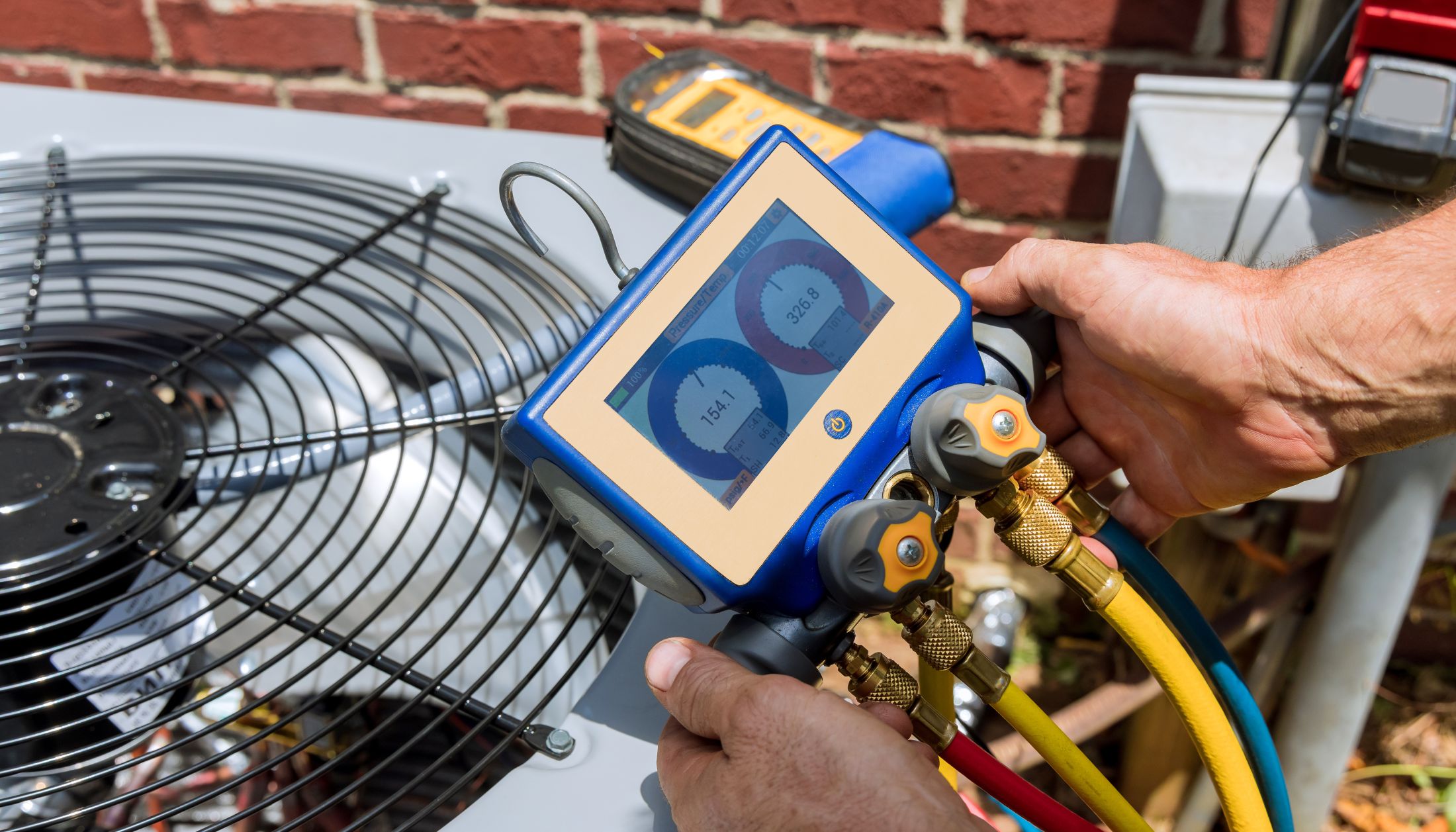 An NCIS technician checking an air conditioner's refrigerant pressures with digital manifold gauges during a service call in North Central Iowa.